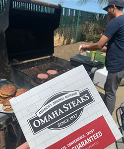 Package of Omaha Steaks held in front of person grilling burgers